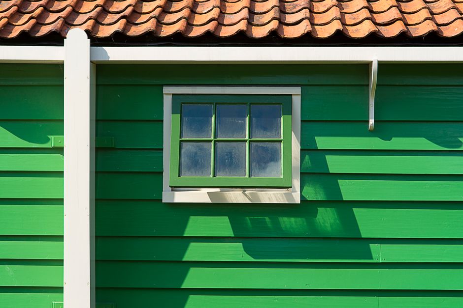 Green painted wooden house with a small window and a tile roof.